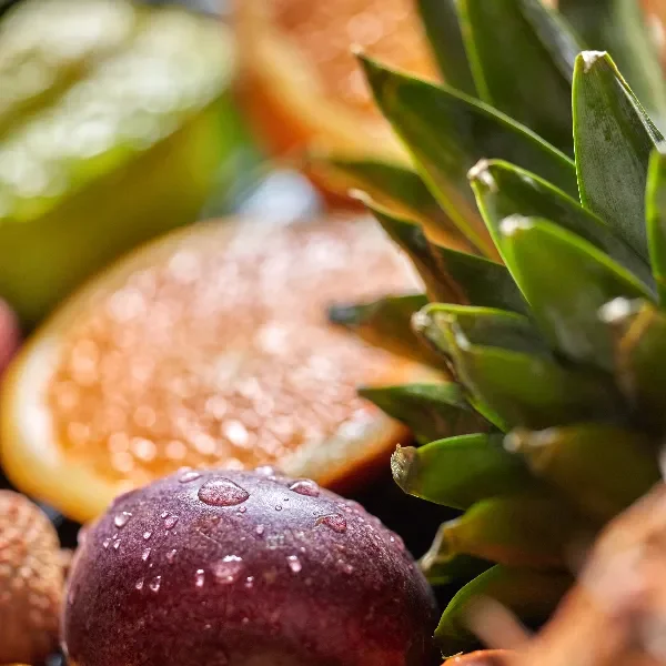 Close-up of fresh, dewy fruit including a plum and pineapple with citrus slices in the background.