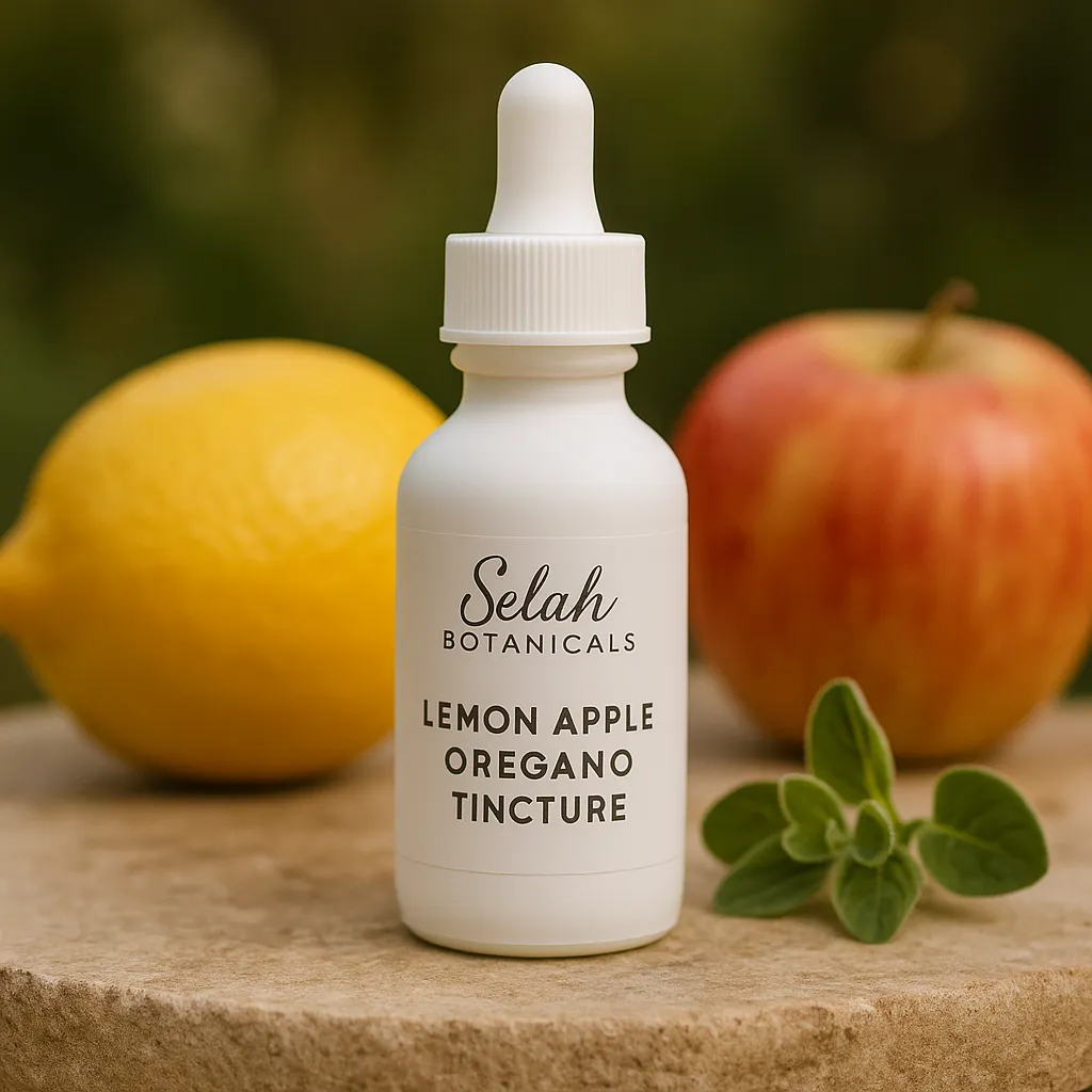 A dropper bottle labeled "Selah Botanicals Lemon Apple Oregano Tincture" is placed on a surface with a lemon, an apple, and oregano leaves in the background.