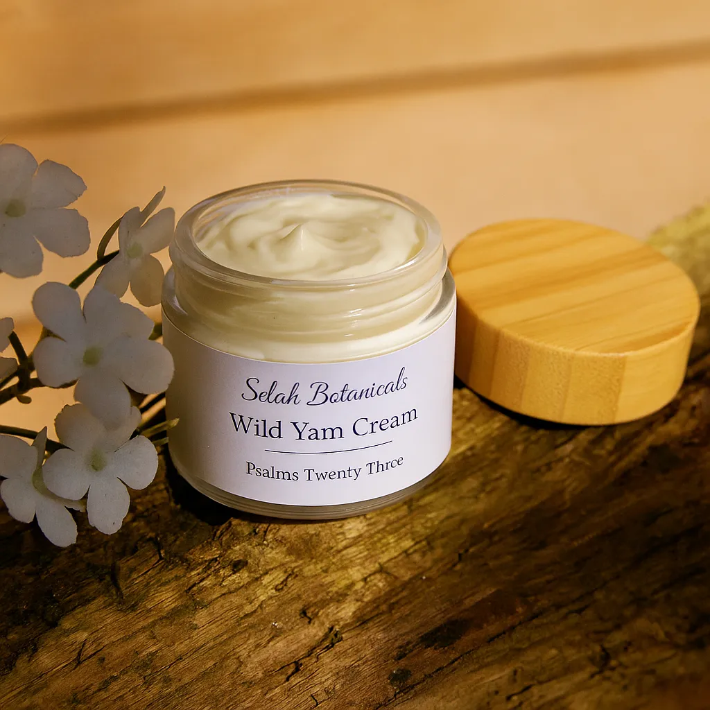 An open jar of Selah Botanicals Wild Yam Cream with a wooden lid resting on a log beside white flowers, in natural sunlight.
